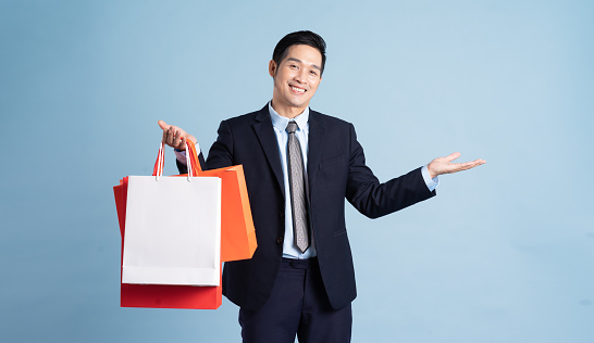 Asian businessman male portrait holding shopping bag on blue background