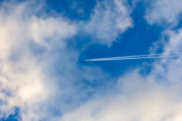 silver plane with vapor trails high in cloudy sky stock photo