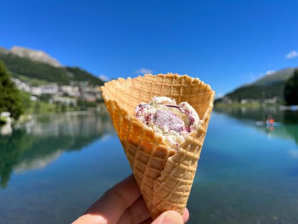 istock Hand holding ice-cream cone, St. Moritzersee and Alpine resort St. Moritz in the background. Graubuenden, Grisons, Switzerland. 1453477406