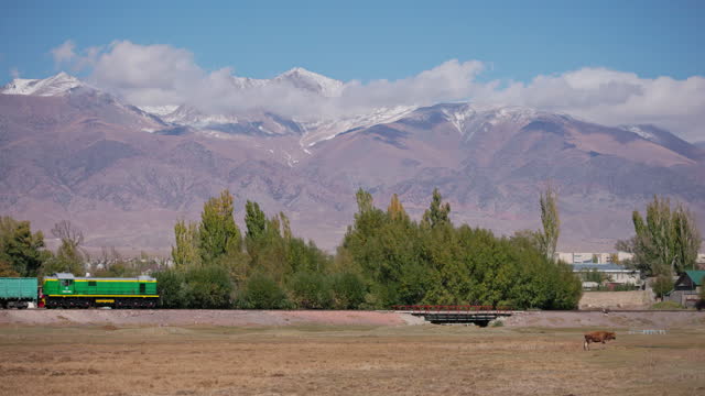train moves in front of Tian Shan mountains at sunny day