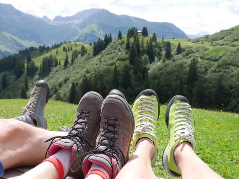 Close up of legs relaxing in meadow, mountains of Arlberg region in the background. Lech, Vorarlberg, Austria.