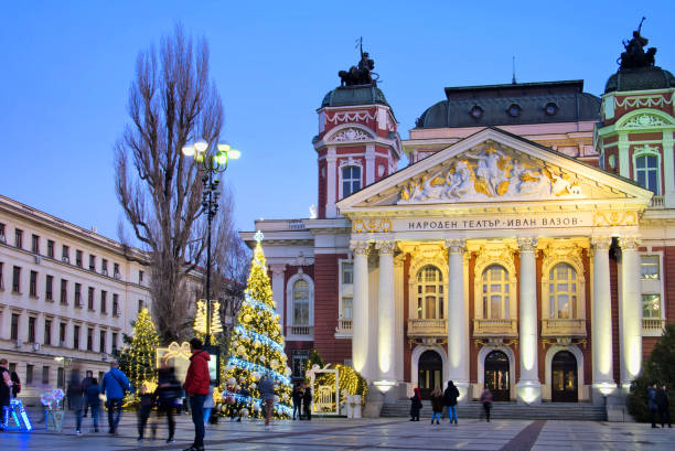 Sofia, Bulgaria, City garden - December 31, 2022: People take a selfie in front of Outdoor Christmas tree and Christmas lights,  in front of National Тheater of Bulgaria in Sofia City garden.