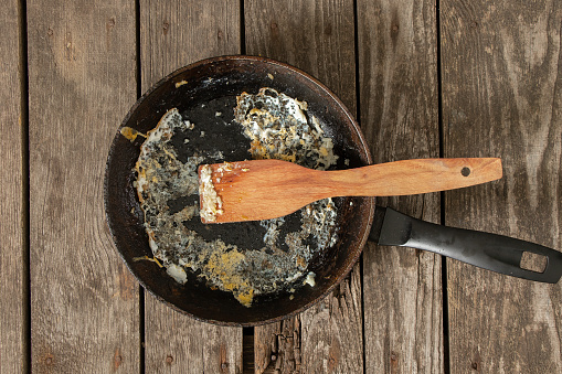 frying pan with food leftovers on a wooden table after breakfast in the kitchen at home
