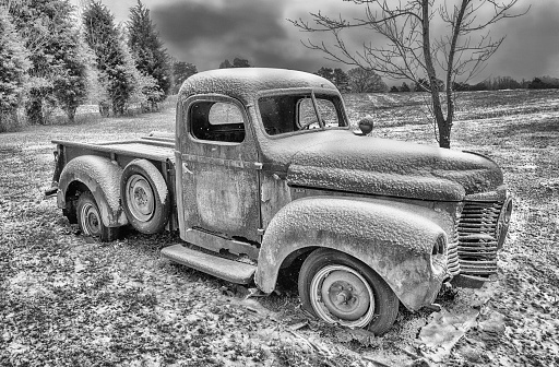 A black & white photo of an old abandoned 1940s era IH pickup sitting in a field with snow.