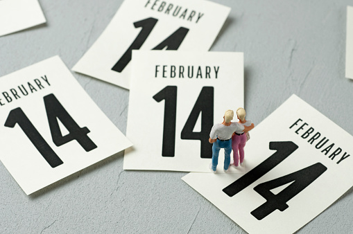 Young couple figurines looking at calendar leaves. February 14 concept.