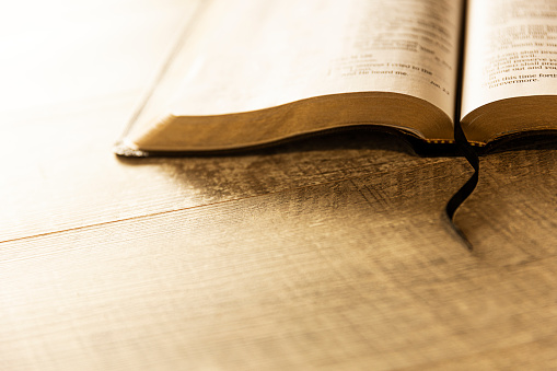 Open book or Bible on highly polished wood table.  Black background.  Reflection in table and there is a satin bookmark inside the book.