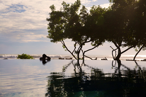 The silhouette of a person looking out of from an infinity pool at the edge of a beach.