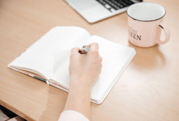 gros plan des mains d’une femme écrivant dans un bloc-notes posé sur une table en bois, un ordinateur portable, un bureau à domicile et un concept de travail, des plans et des pensées - interview meeting business women photos et images de collection