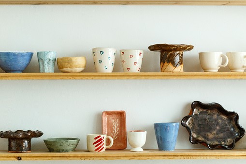 Handmade ceramic crockery and craft pottery jug, jars and cups standing on shelves, creative studio or potter store. Different handicraft clay earthenware bowls in artisan craftsman classes workshop