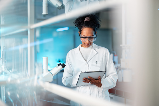Portrait of a young Hispanic chemist writing down the results in her diary. Determined researcher standing by microscope in laboratory.