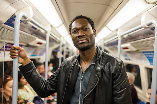 Waist up portrait of a serious mature African American man standing in a subway metro. He is looking at the camera and wearing a leather jacket.