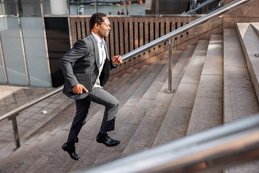 Mature African American male in a hurry to get on time to a business meeting. He is wearing formal businesswear and carrying a digital tablet.