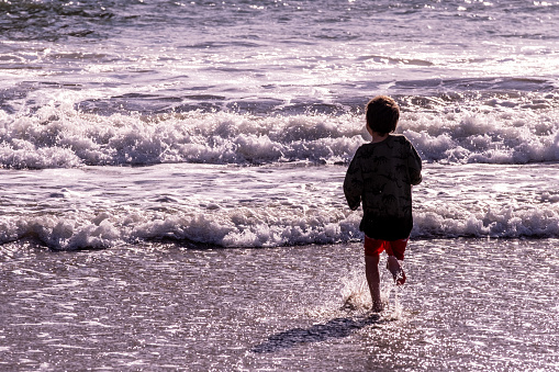 Caucasian Little boy running at the beach, breaking waves, sea, ocean