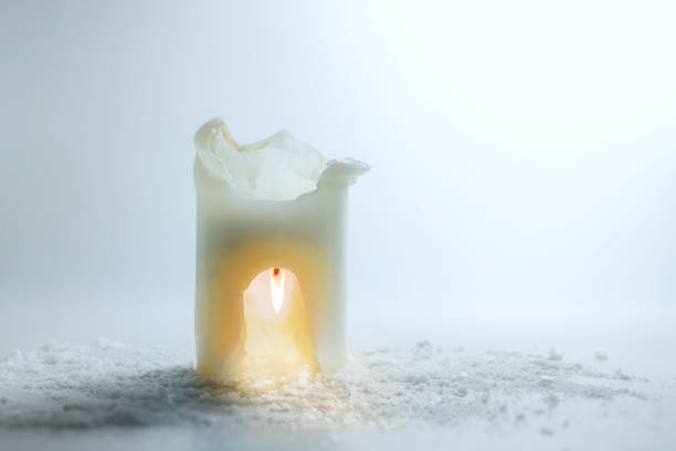 White candle is burning upside down in a carve, saving heat and energy concept, surreal winter holiday still life, light gray background, copy space, selected focus stock photo