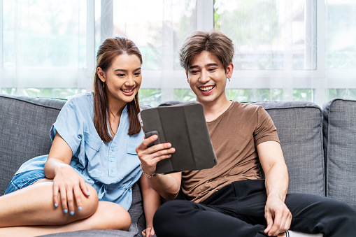 Portrait of an happy couple in love using a tablet, looking at digital computer tablet screen, relaxing on comfortable couch. Loving couple shopping online in internet store.
