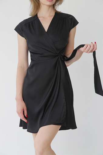 Serie of studio photos of young female model in black silk satin wrap mini dress.