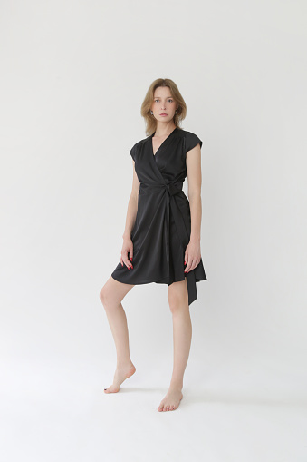 Serie of studio photos of young female model in black silk satin wrap mini dress.
