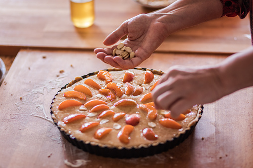 French cuisine, Apricot Frangipane Tart preparing, sprinkling flaked almond, close up, selective focus on hand holding almonds