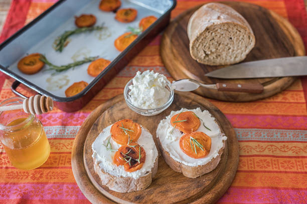 Healthy breakfast, bread slices  with soft cheese sweet spread, honey and fresh baked apricot halves on table, close up, no people