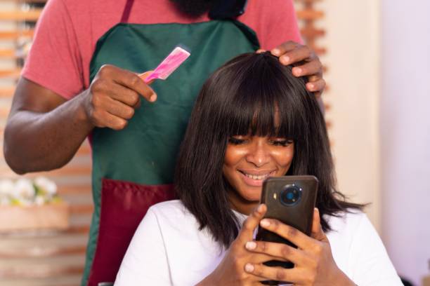 giovane donna nigeriana in un parrucchiere che usa il suo telefono - owner hair salon beauty spa female foto e immagini stock
