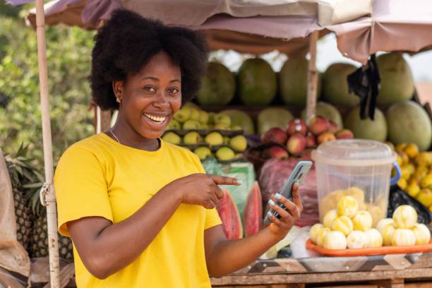 istock Happy African market woman using her phone and points to it 1453568524