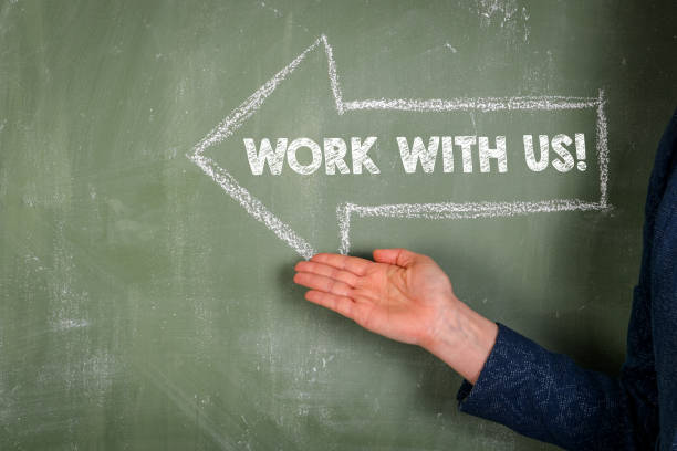 istock Work with us. Text and white pointing arrow on green chalkboard 1453568841