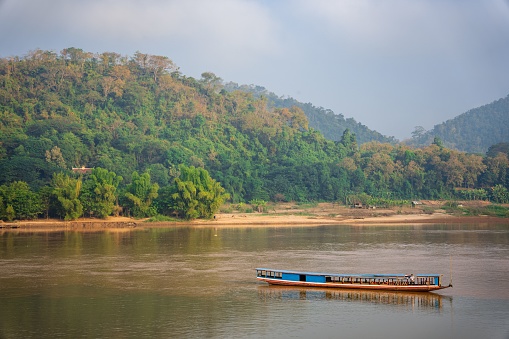 A beautiful shot of the Mekong River with a floating boat near mountains in Luang Prabang, Laos