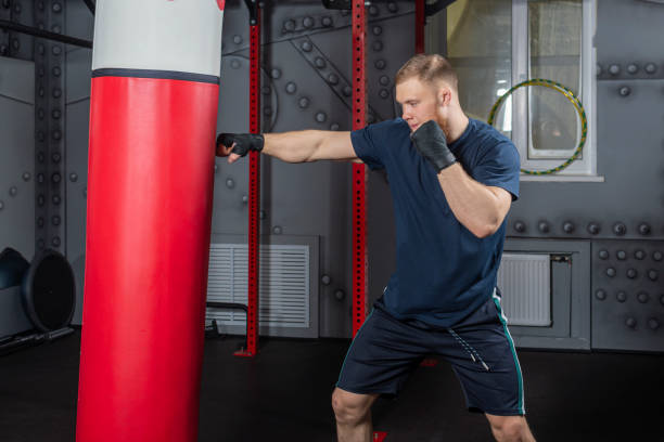 istock Young and strong mixed martial arts fighter practices punches with his right hand on punching bag 1453569767