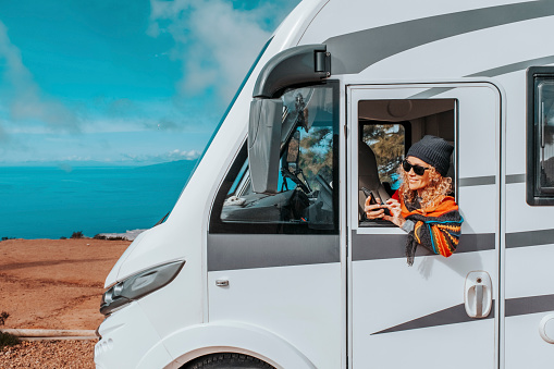 One woman enjoy arrival vacation travel destination after drive a big camper van motor home. Concept of happy female people in van life lifestyle. Summer journey. Planning road trip on mobile phone