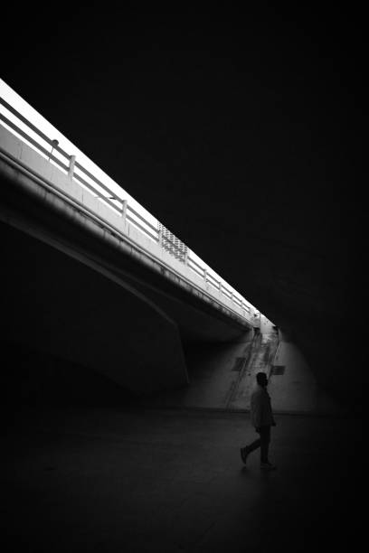 istock Grayscale of a man walking on a pedestrian walkway under a bridge 1453569930