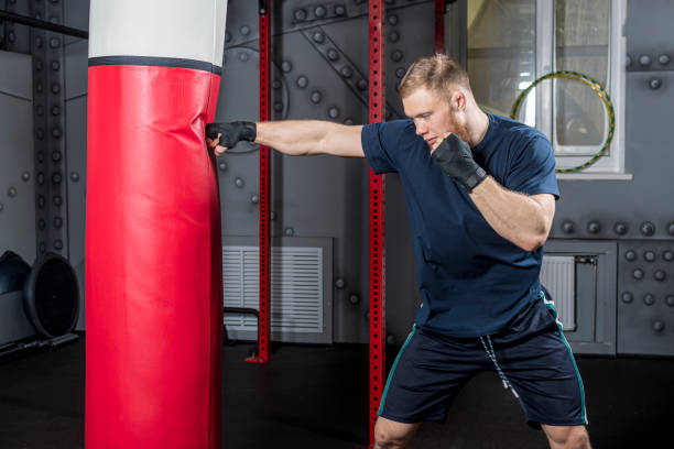 istock Young and strong mixed martial arts fighter practices punches with his right hand on punching bag 1453569954