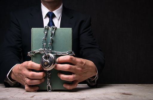 A businessman wearing a suit holding a book wrapped in chain and a lock