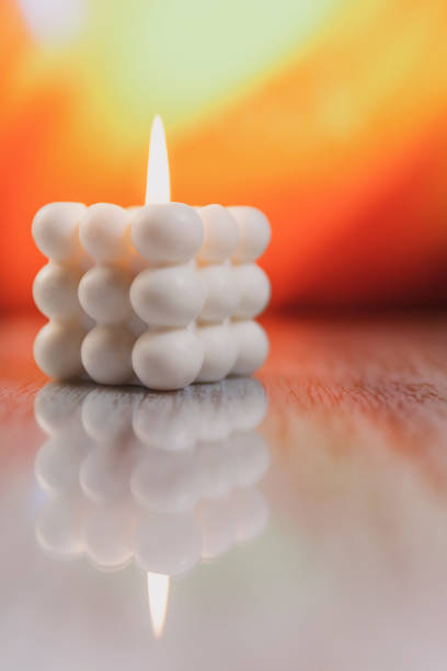 A vertical shot of a decorative burning white cubed candle on an orange background