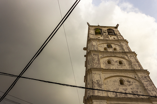Low angle view of the ancient tower at the 18th century Masjid Kampang Kling mosque against a cloudy sky in the city of Malacca in Malaysia.