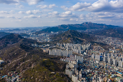 An aerial cityscape of Seoul surrounded by buildings in background of mountains