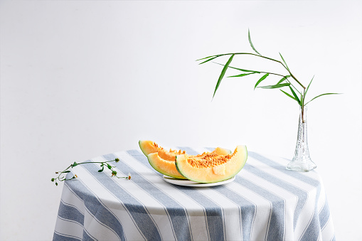 A still life photo of melon slices on a round table and bamboo leaves in a vase