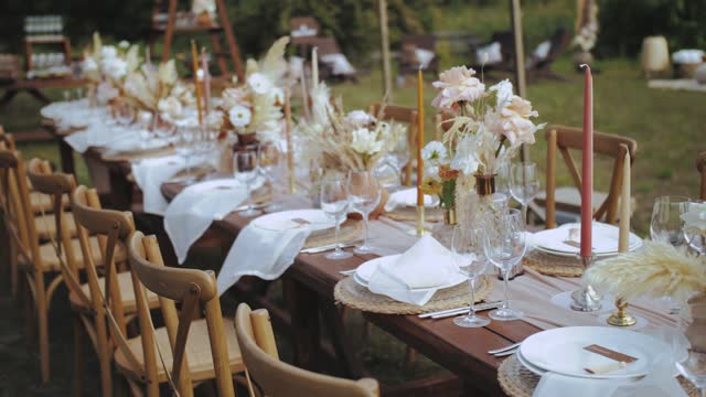 Close-up table served and decorated with candles and dried and pastel flowers for boho style wedding dinner, plates and wine glasses, no people shot, slow motion.