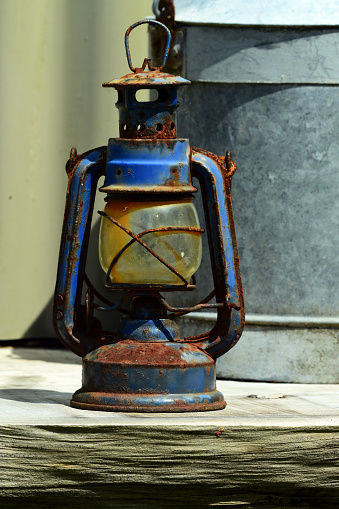 Old rusty kerosene lamp stands on a table.