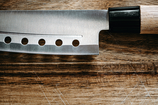 Sharp knife's blade on cutting board. Brushed stainless steel material