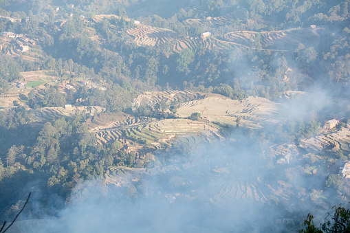Nepal's terraced cropland in winter and the smoke of burning fires wafting into the sky