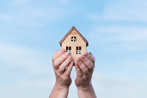 istock House in hands on the blue sky with clouds 1453591404