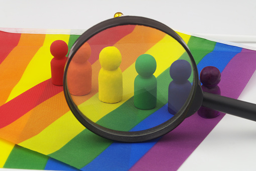 LGBT people review concept. Many people figures rainbow colored on LGBT pride flag under magnifying glass isolated on white.