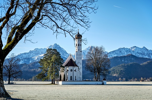 The St. Coloman church in Schwangau, Germany surrounded by forests and snowy mountains on a sunny day