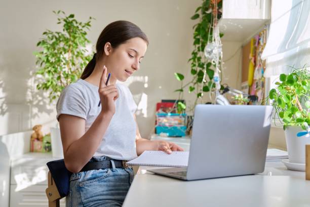 istock Teenage girl studying at home using laptop making notes in notebook 1453593007