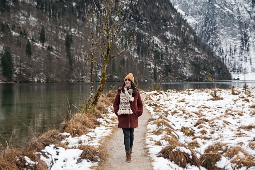 An adventurous girl in a brown coat and scarf walking on a trail at Lake Konigssee in Bavaria, Germany