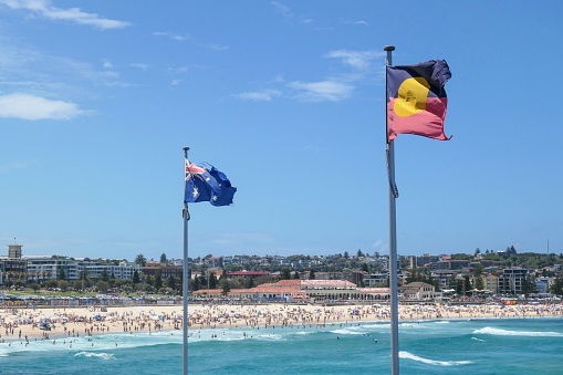 The Australian and Australian Aboriginal flags fly with the background of Bondi Beach, Sydney, on New Year's Day 2023.  This image was taken on a sunny afternoon in summer.