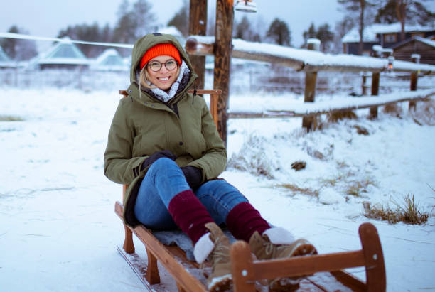 istock Smiling woman sitting on a sled and looking directly at the camera 1453596811