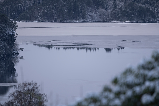 Early morning winter landscape at a fjord (Nordasvannet) near the City of Bergen on the west coast of Norway. The seawater of the fjord is partly frozen and covered with snow. The image was captured on an overcast and cloudy day.