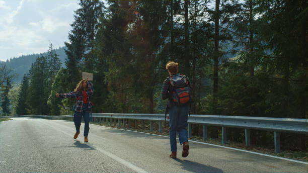 istock Backpackers standing mountain road outdoors. Hitchhikers wave hands on holiday. 1453605919