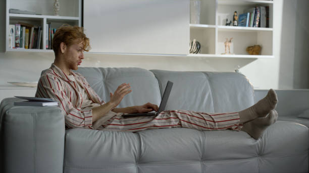 istock Freelancer talking home online resting in pajamas. Ginger man working remotely 1453613292
